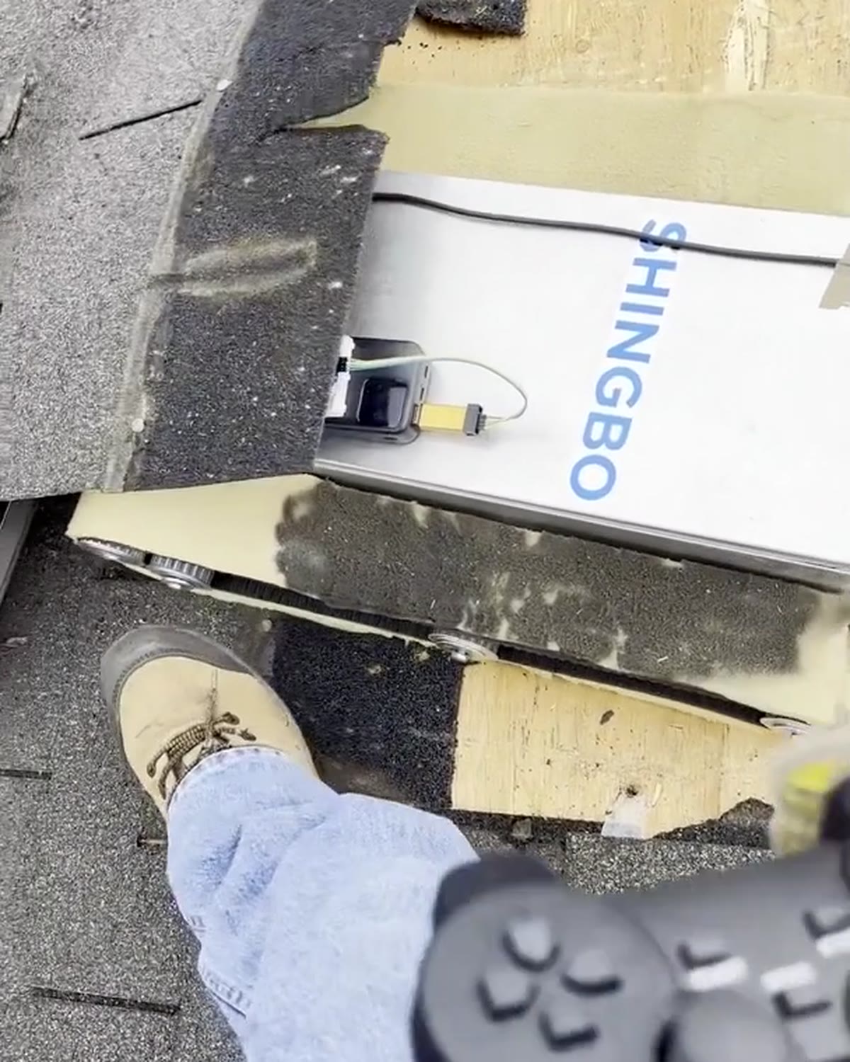 A roofing crew member operating the Shingbo tear-off robot with a handheld controller